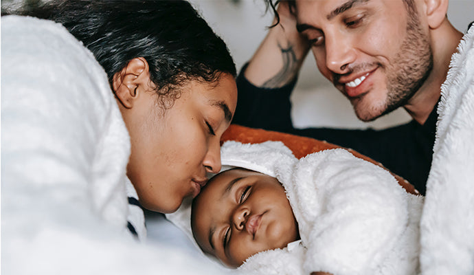 Parents snuggling with their sleeping baby.